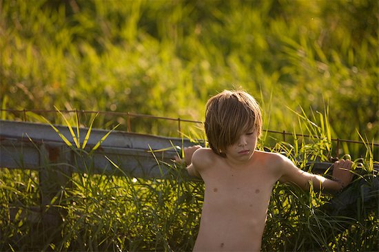 Boy leaning on fence in field.jp