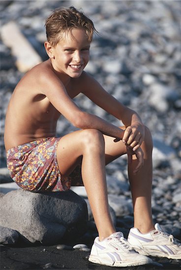 Boy sitting on rock at pebbled b