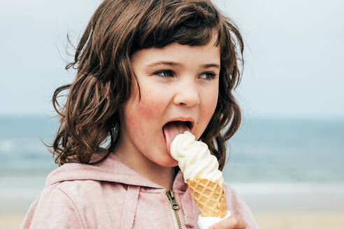 girl-with-dark-hair-looking-away-and-licking-ice-cream-while-spe