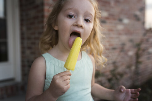 portrait-of-girl-eating-popsicle-stick-while-standing-against-ho